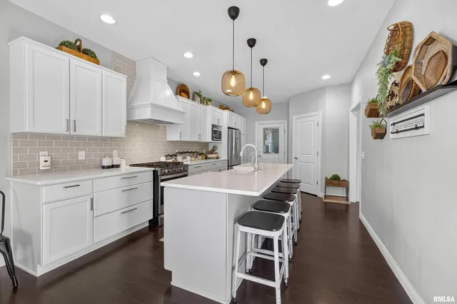 a open kitchen with stainless steel appliances granite countertop a stove top oven a sink a dining table and chairs with wooden floor