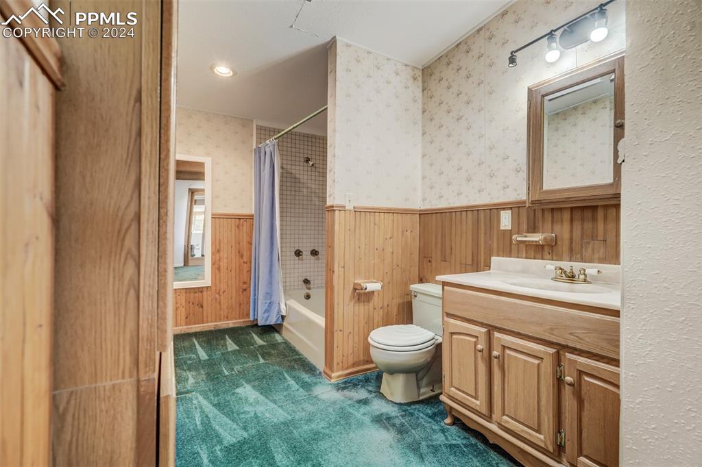 23555 Murphy Road Calhan, CO 80808 - Photo 39 of 49 Full bathroom with vanity, wooden walls, shower / bath combo with shower curtain, and toilet