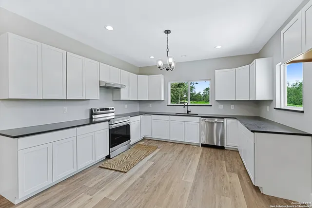 a white kitchen with wooden floor stainless steel appliances and cabinets