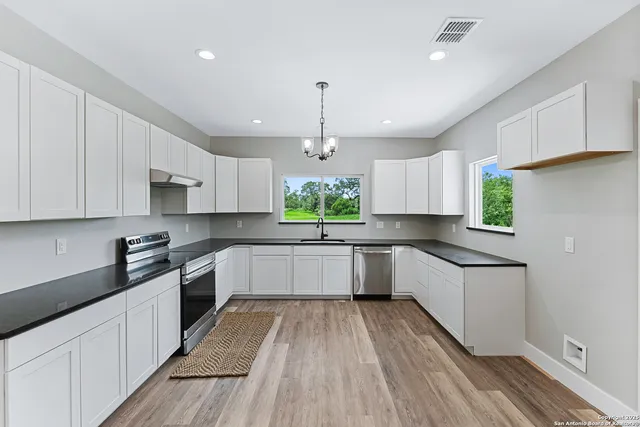 a kitchen with granite countertop a white stove top oven sink and cabinets with wooden floor