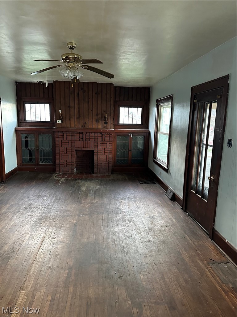 37 Fairview Road Chester, WV 26034 - Photo 2 of 11 Unfurnished living room with a fireplace, wooden walls, a healthy amount of sunlight, dark wood-type flooring, and ceiling fan