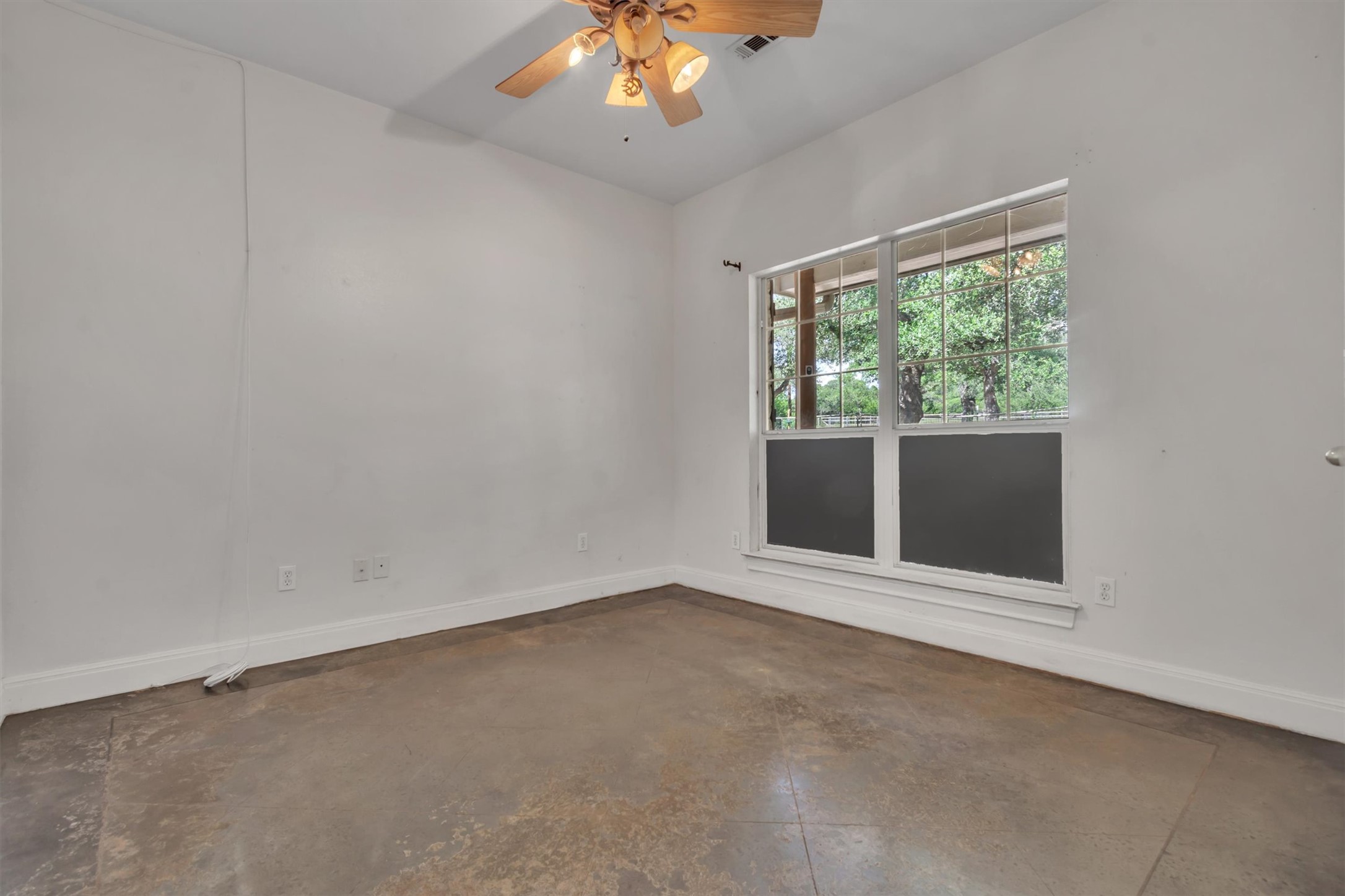 1120 Meadow Ridge Drive Austin, TX 78737 - Photo 21 of 40 A well-lit room featuring concrete flooring, a large window with outdoor views, and a classic ceiling fan.