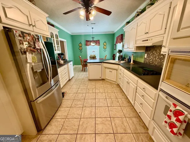 a kitchen with stainless steel appliances granite countertop a refrigerator a sink and white cabinets