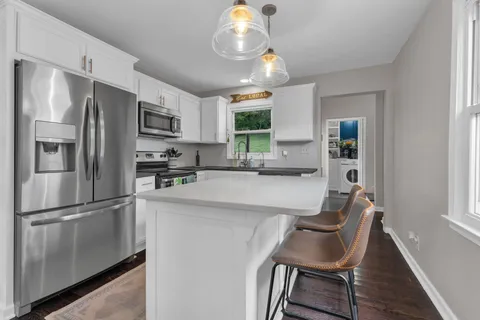 a kitchen with stainless steel appliances granite countertop a refrigerator a microwave a stove and white cabinets with wooden floor