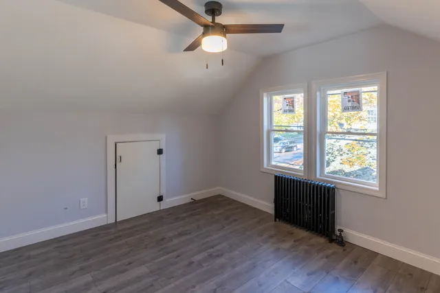 an empty room with wooden floor chandelier fan and windows