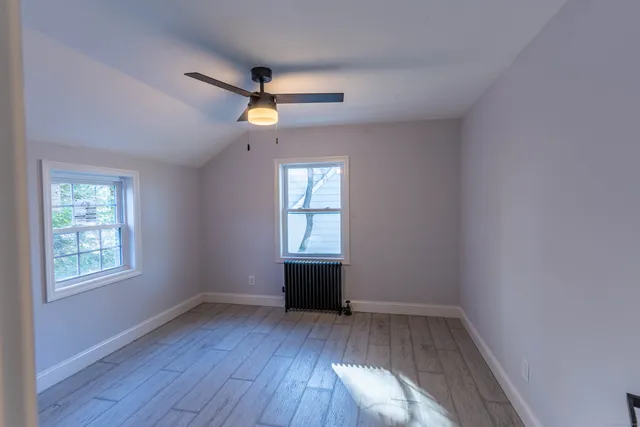 an empty room with wooden floor ceiling fan and windows