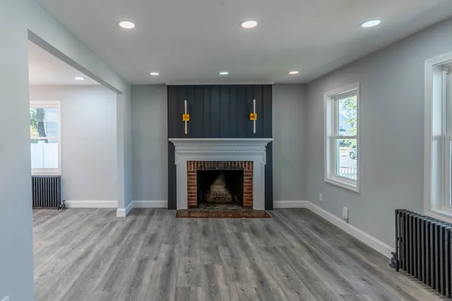 a view of an empty room with wooden floor fireplace and a window