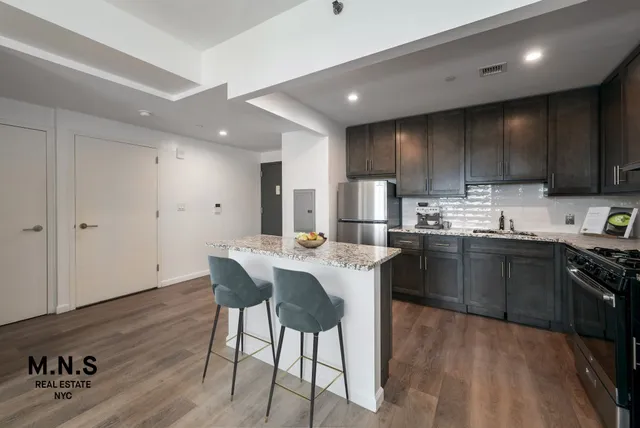 a kitchen with stainless steel appliances kitchen island granite countertop a sink a stove a refrigerator and a microwave with wooden floor