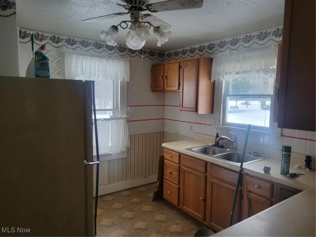 7631 Mines Road Southeast Warren, OH 44484 - Photo 4 of 22 Kitchen featuring refrigerator, brown cabinetry, light countertops, a textured ceiling, and a ceiling fan