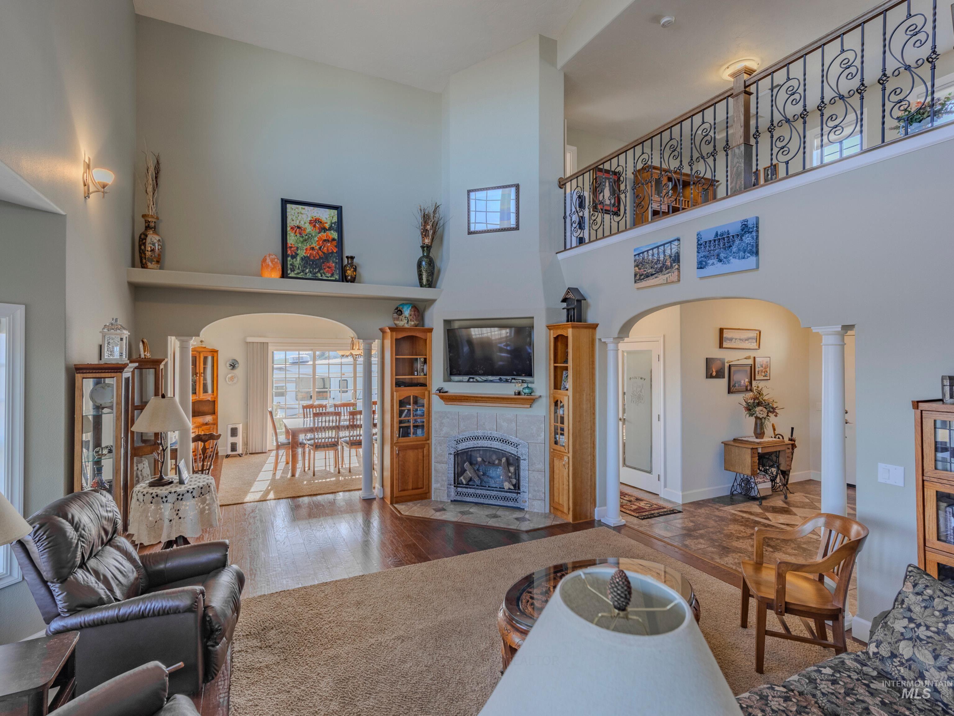 659 Reservation Line Road Cottonwood, ID 83522 - Photo 10 of 50 Living area featuring arched walkways, wood-type flooring, a tile fireplace, a high ceiling, and ornate columns