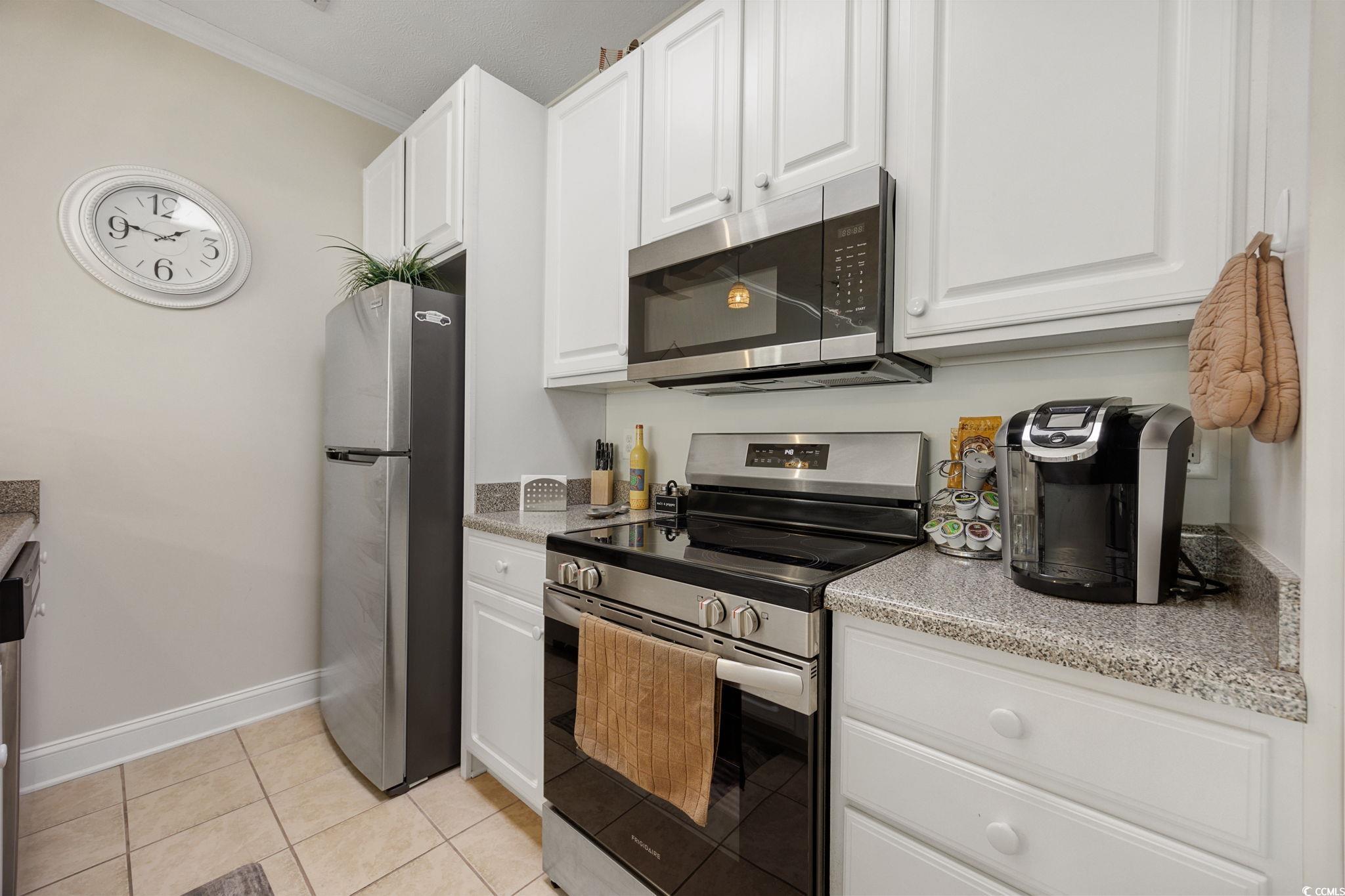 121 Waypoint Ridge Avenue, Unit P8 Little River, SC 29566 - Photo 5 of 40 Kitchen with appliances with stainless steel finishes, white cabinetry, ornamental molding, light tile patterned floors, and light stone countertops