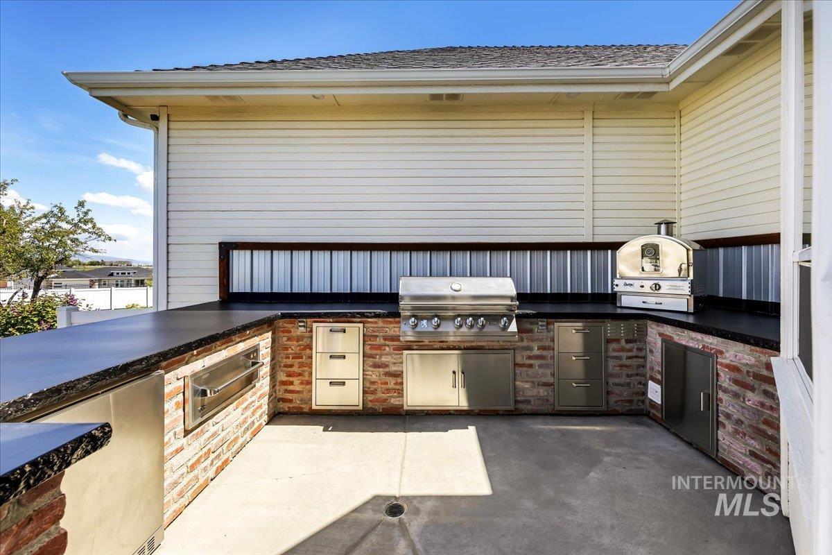 414 East Shafer View Drive Meridian, ID 83642 - Photo 46 of 50 Expansive outdoor kitchen featuring a built-in stainless steel grill w/rotisserie, permanent gas line, integrated storage drawers, a warming drawer, undercounter refrigerator and durable brick and concrete constructed breakfast bar has barstool seating!