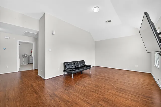 a view of an empty room with wooden floor and a way to kitchen