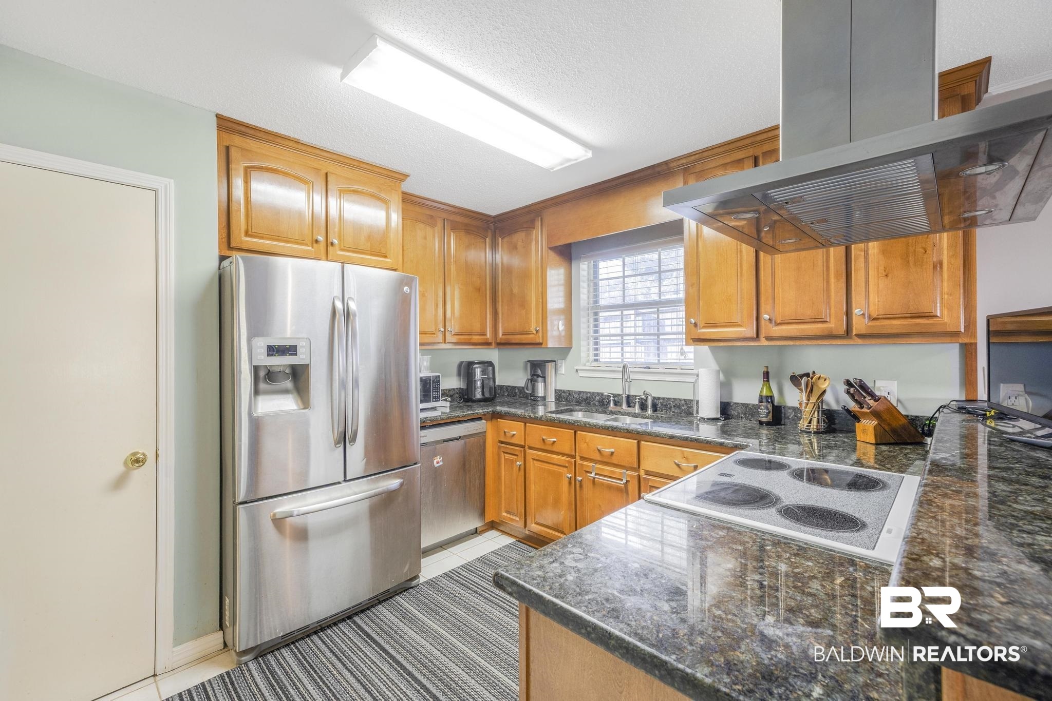 2573 E Road Mobile, AL 36693 - Photo 5 of 45 Kitchen featuring stainless steel appliances, exhaust hood, dark stone countertops, brown cabinetry, and a textured ceiling