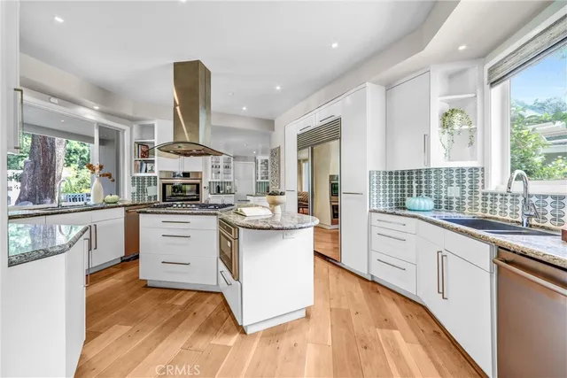 a kitchen with stainless steel appliances kitchen island granite countertop a stove a sink dishwasher and white cabinets with wooden floor