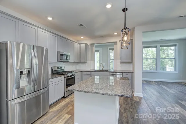 a kitchen with granite countertop kitchen island stainless steel appliances a refrigerator cabinets and wooden floor