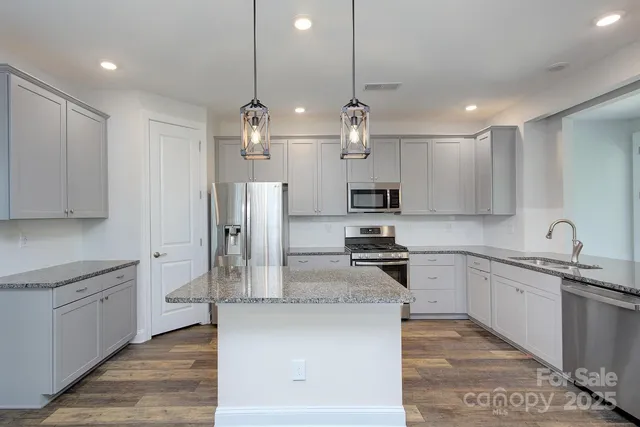 a kitchen with stainless steel appliances granite countertop a sink a stove a refrigerator and island with wooden floor