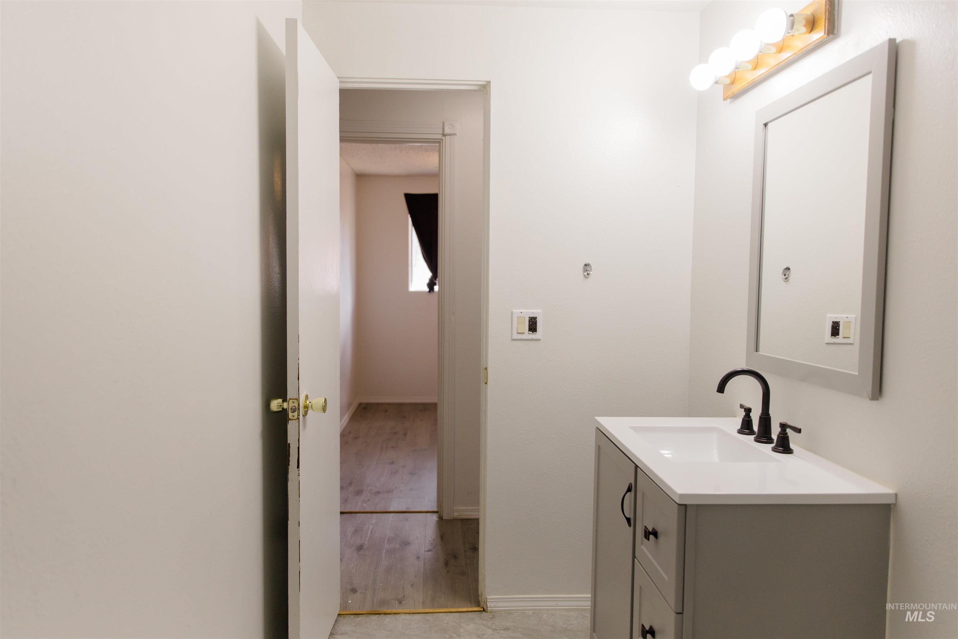 1230 East 17th North Mountain Home, ID 83647 - Photo 5 of 27 White cabinetry, black marble-look countertops, stainless steel dishwasher, wood-finish flooring, and a double basin sink