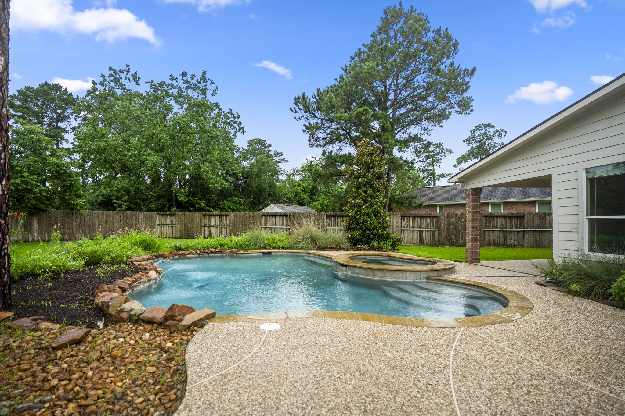 6311 Sparrows Glen Lane Spring, TX 77379 - Photo 36 of 50 Curved pool lines, an elevated spa, and layered planting beds create a backyard that feels relaxed but polished, with the patio wrapping along the home and no rear neighbors behind the fence.