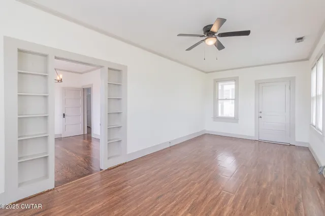 a view of an empty room with a window and wooden floor