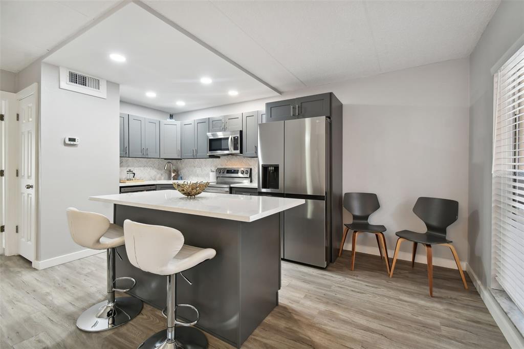 8901 Blind Pass Road, Unit 228 St. Pete Beach, FL 33706 - Photo 8 of 29 a kitchen with stainless steel appliances granite countertop a dining table chairs refrigerator sink and cabinets