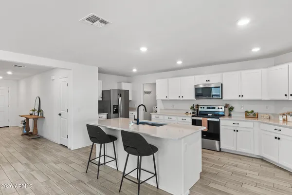 a kitchen with stainless steel appliances kitchen island granite countertop a stove a sink a refrigerator and white cabinets with wooden floor