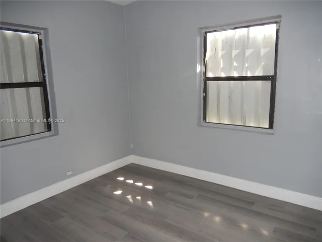 a view of an empty room with wooden floor and window