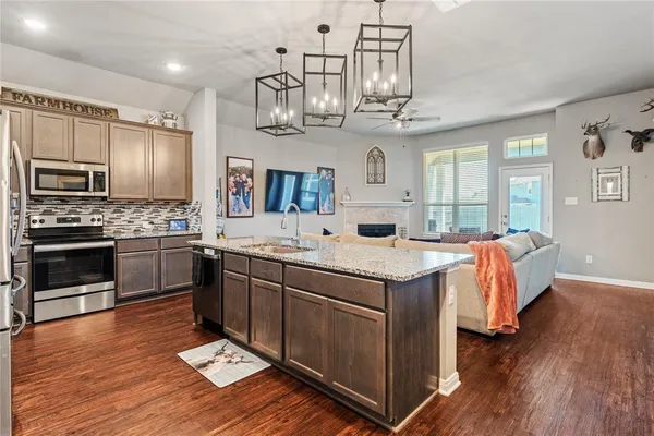 a kitchen with stainless steel appliances a stove a sink dishwasher a refrigerator and a fireplace with wooden floor