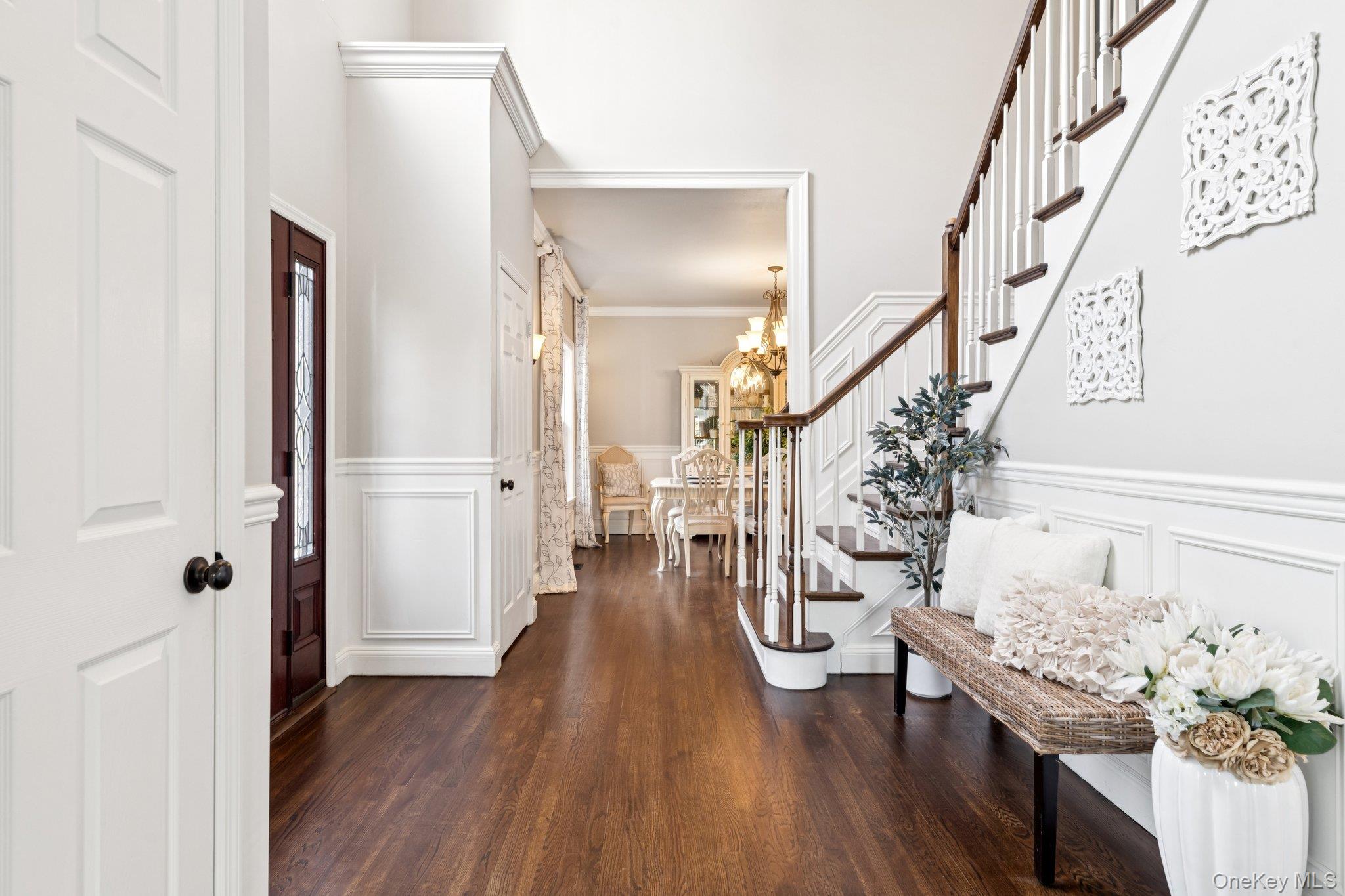 7 Brittany Court Ridge, NY 11961 - Photo 11 of 45 Entrance foyer with stairs, a chandelier, dark wood-style floors, a decorative wall, and wainscoting