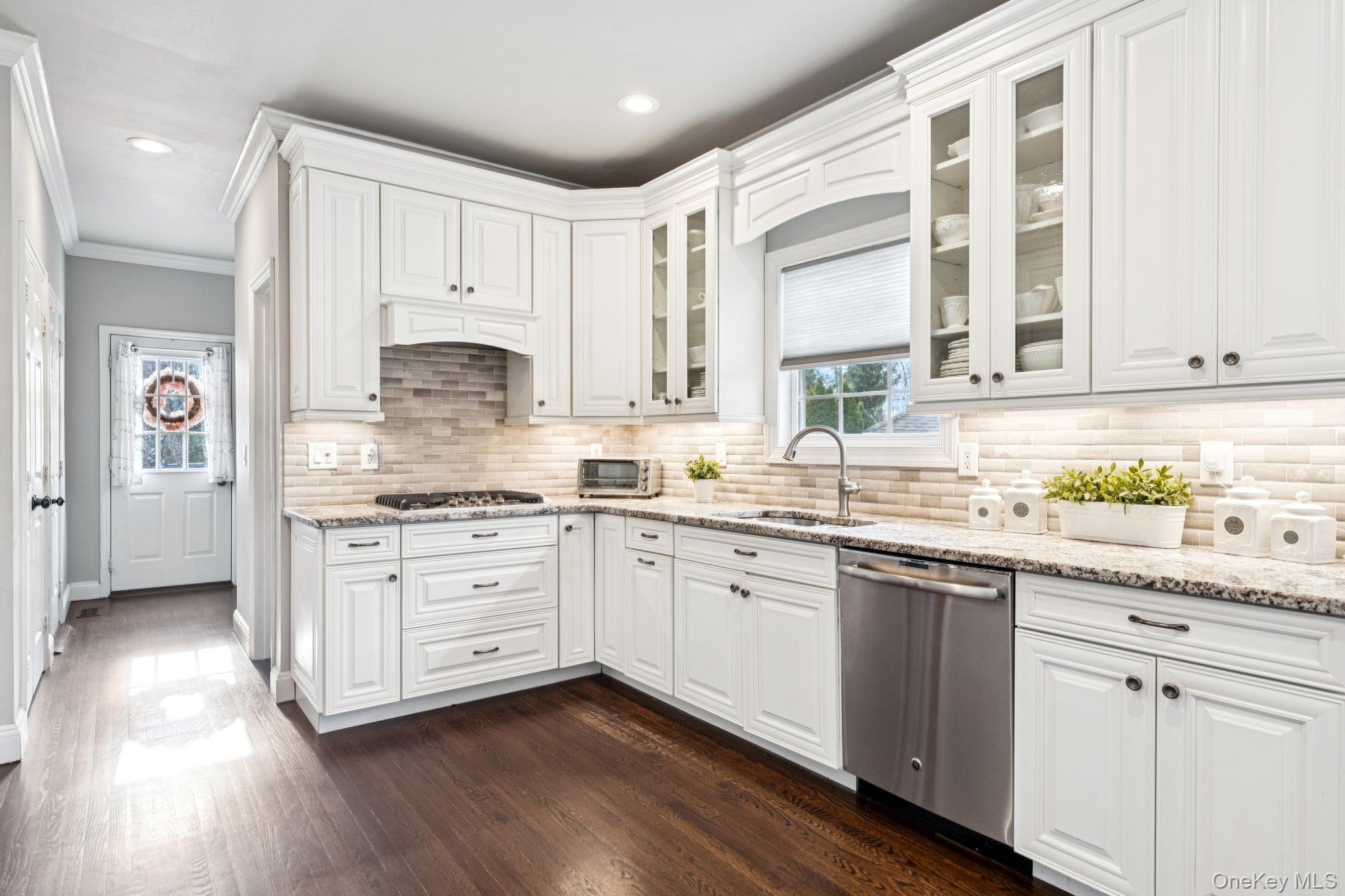 7 Brittany Court Ridge, NY 11961 - Photo 21 of 45 Kitchen featuring white cabinets, light stone counters, ornamental molding, appliances with stainless steel finishes, and dark wood-type flooring