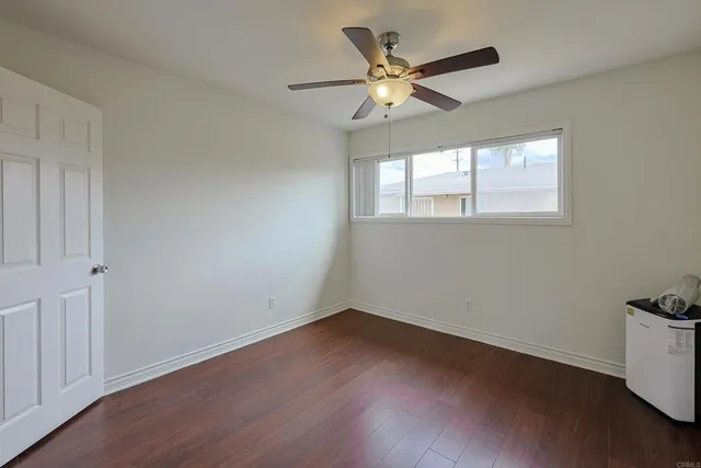 an empty room with wooden floor chandelier fan and windows