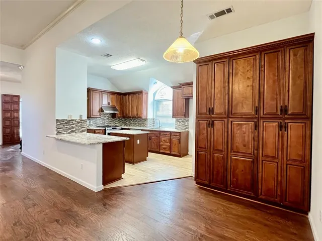 a large kitchen with stainless steel appliances granite countertop wooden floors wooden cabinets a sink and a window