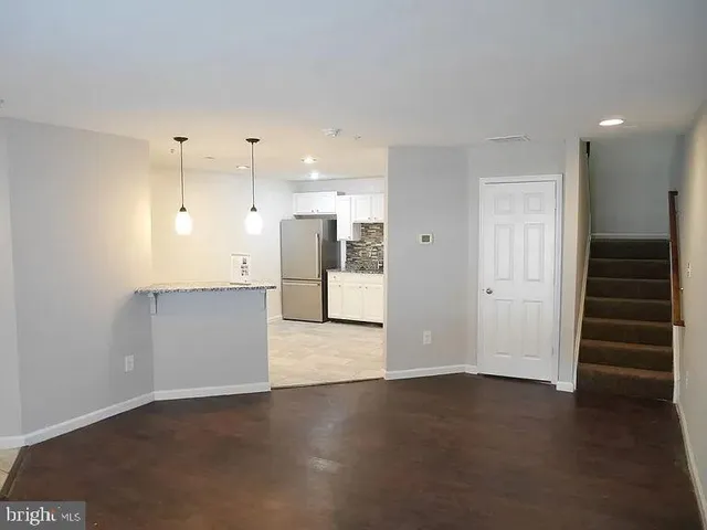 an empty room with wooden floor and a kitchen