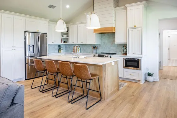 a kitchen with stainless steel appliances a stove a sink dishwasher a refrigerator with white cabinets and wooden floor