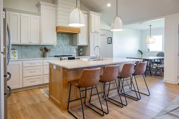 a kitchen with stainless steel appliances granite countertop a stove a sink dishwasher and white cabinets with wooden floor