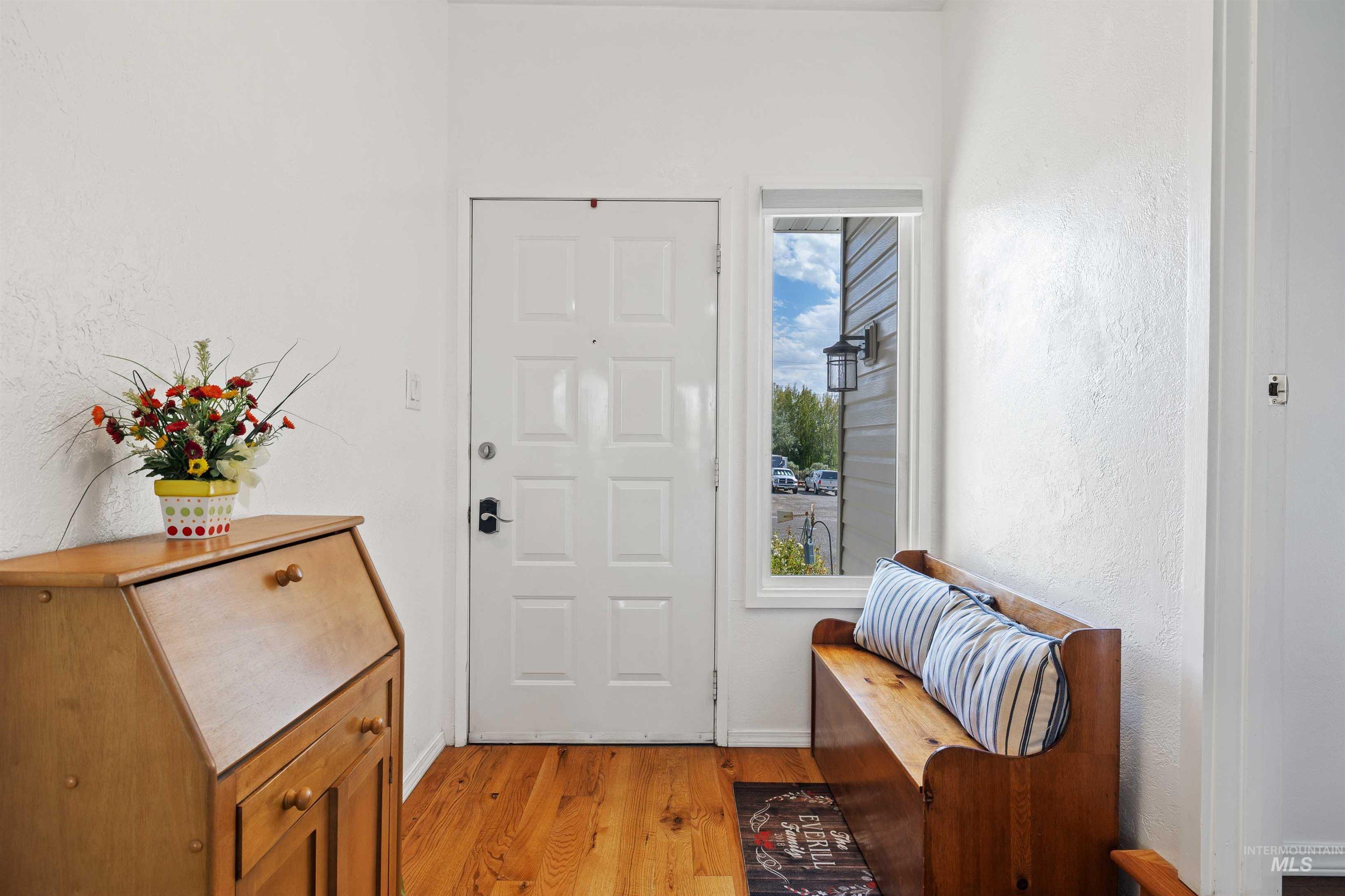 White paneled entry door with sidelight, wood-finish flooring, and white wall finishes