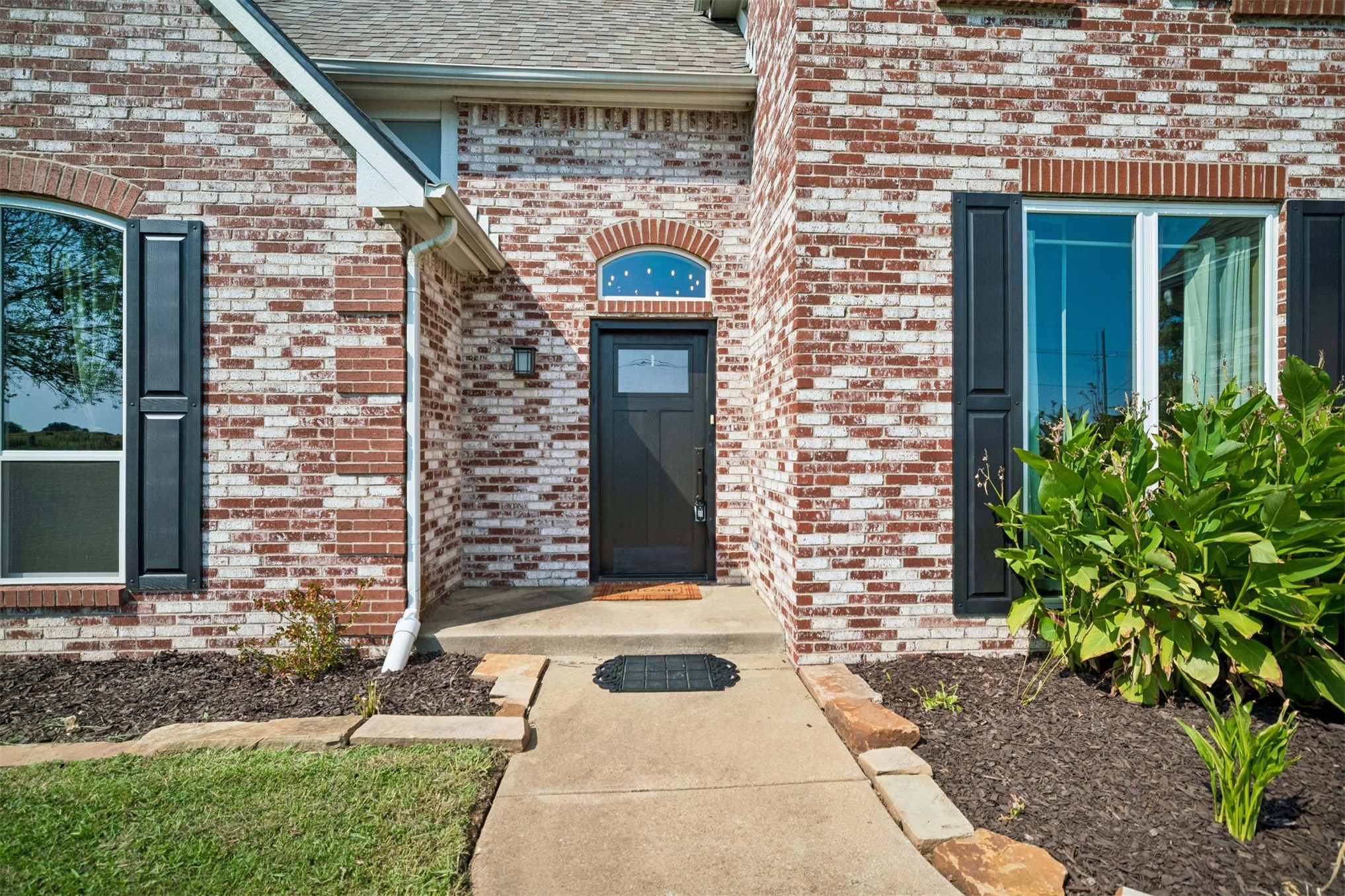 Brick exterior with white mortar, arched and rectangular windows, black decorative shutters, and a dark entry door with an arched transom