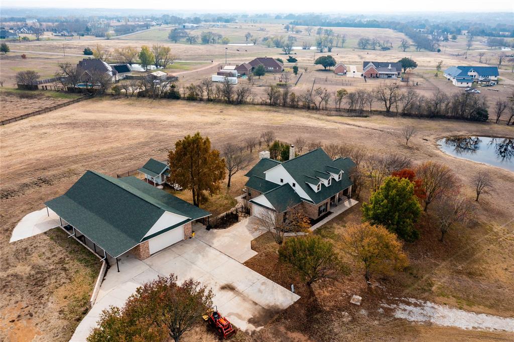 364 Parker Road, Unit A Van Alstyne, TX 75495 - Photo 23 of 39 Expansive property featuring a main residence with dormer windows, a detached auxiliary building with a covered carport, a private pond, mature trees, and a concrete driveway