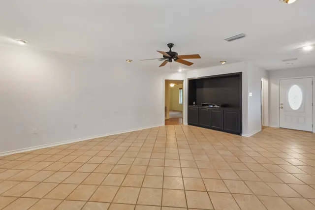 an empty room with chandelier fan and windows