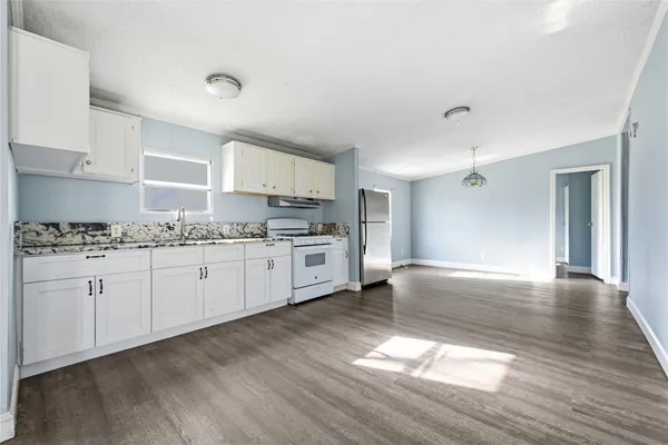 a kitchen with granite countertop a stove a sink and white cabinets with wooden floor