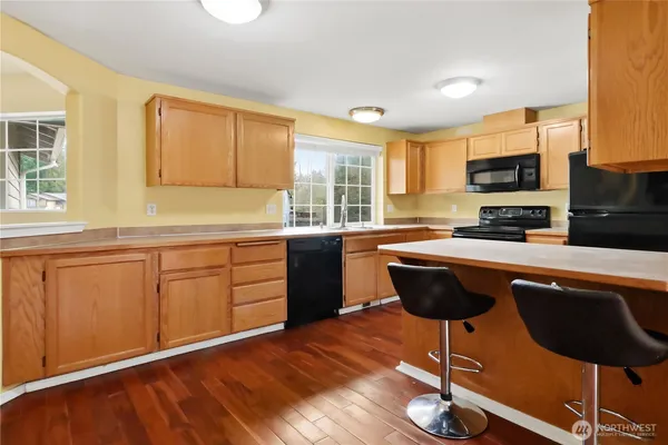 a kitchen with stainless steel appliances granite countertop a stove a sink a microwave a dining table and chairs with wooden floor