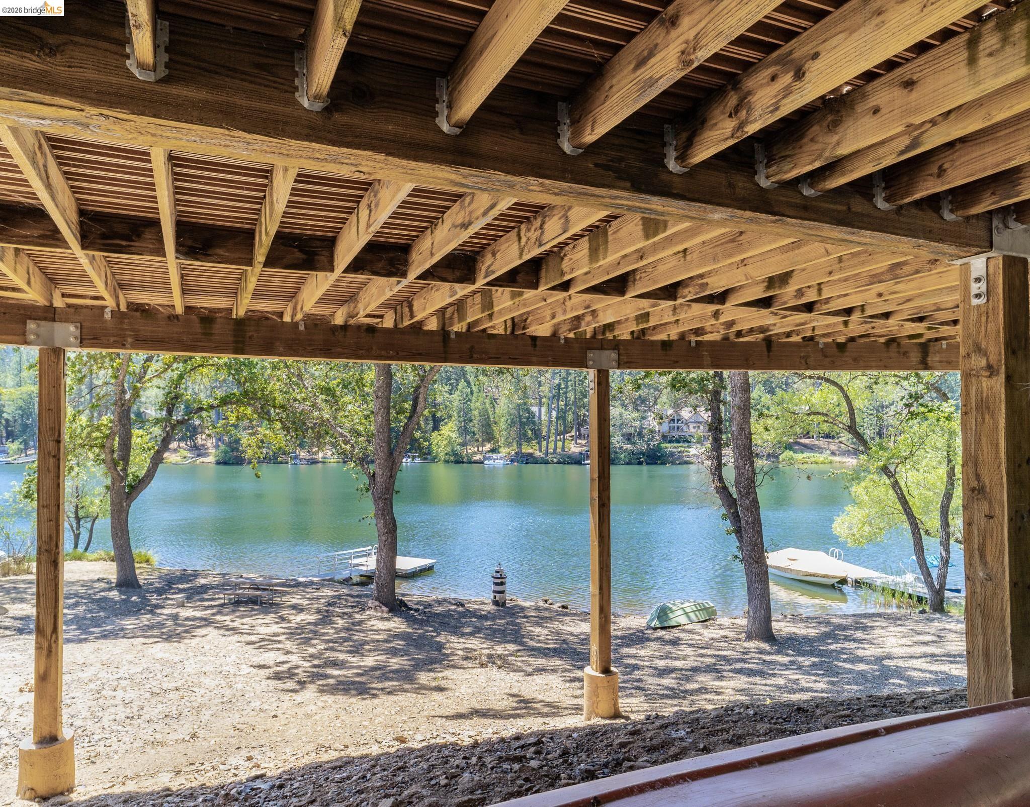 19711 Pleasantview Drive Groveland, CA 95321 - Photo 30 of 39 Covered outdoor space featuring exposed wood joists and support beams, opening to a waterfront setting with mature trees and a dock