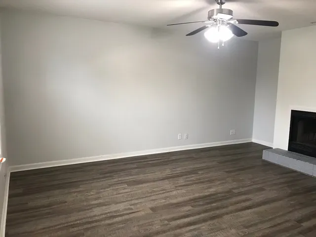 a view of an empty room with wooden floor and a chandelier fan