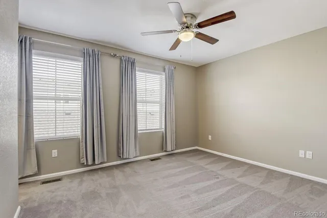 an empty room with chandelier fan and windows