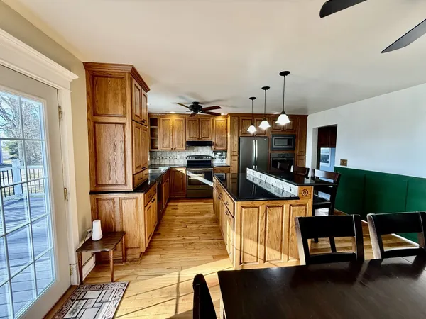 a kitchen with stainless steel appliances granite countertop a stove a refrigerator a sink a dining table and chairs with wooden floor