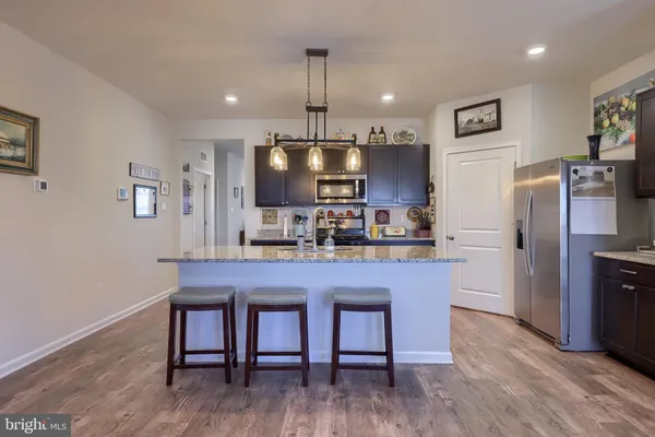 a kitchen with stainless steel appliances granite countertop a refrigerator a sink dishwasher a stove a dining table and chairs with wooden floor