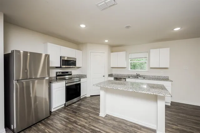 a kitchen with kitchen island granite countertop appliances cabinets and a sink