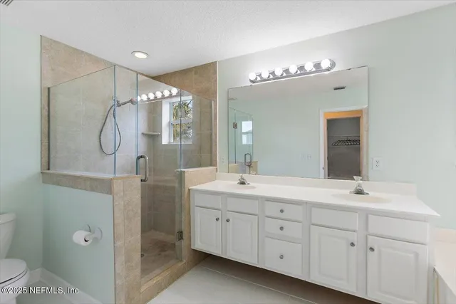 a spacious bathroom with double sink a toilet a shower and a mirror