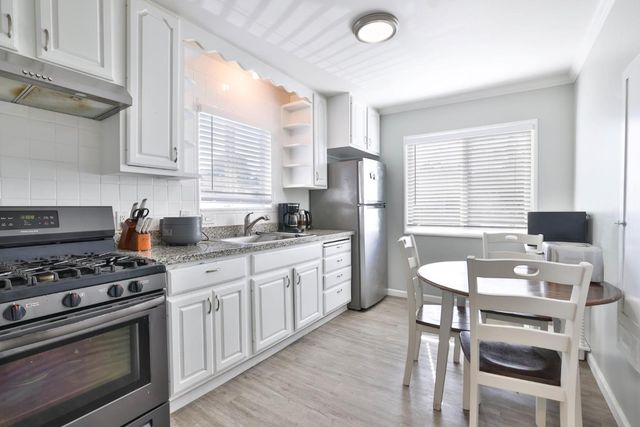 a kitchen with stainless steel appliances granite countertop a stove a sink dishwasher a refrigerator with white cabinets and wooden floor