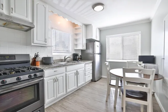 a kitchen with stainless steel appliances granite countertop a stove a sink dishwasher a refrigerator with white cabinets and wooden floor